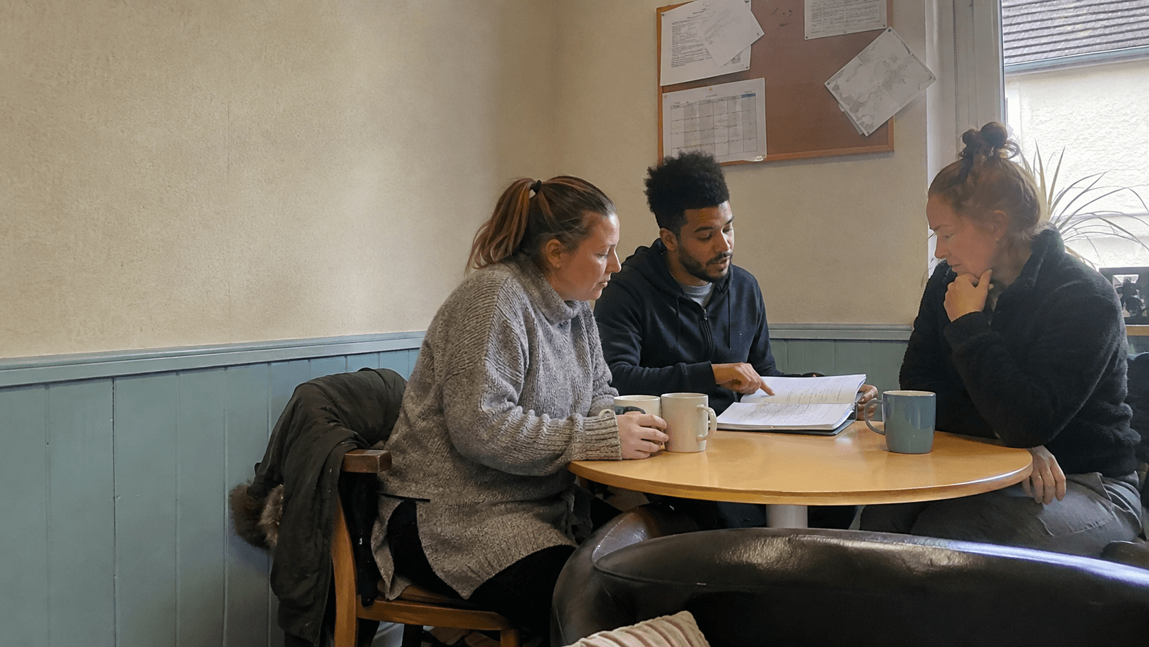 Three support workers discussing notes during a team handover.