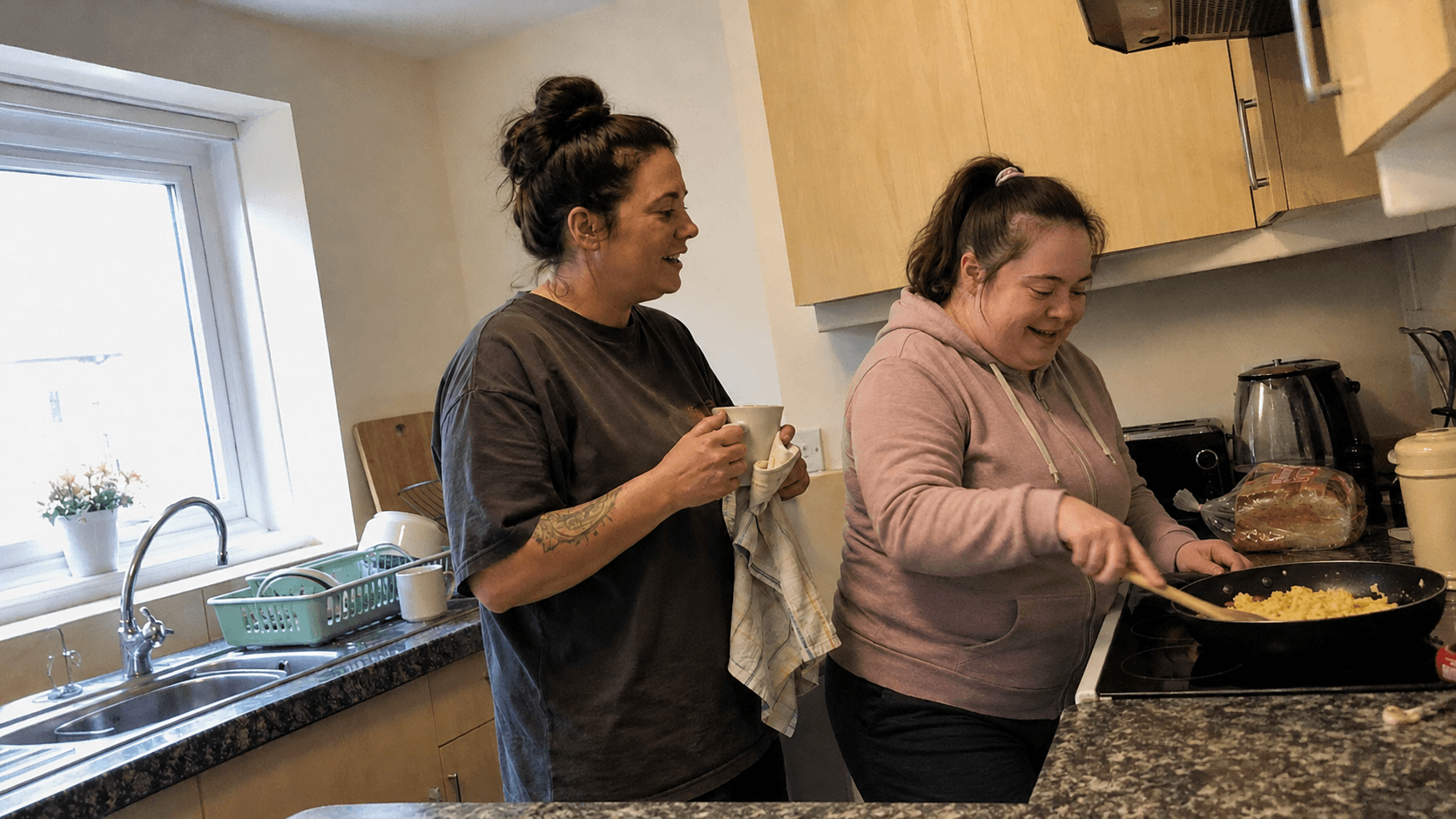 An adult preparing food with a support worker in an everyday kitchen.
